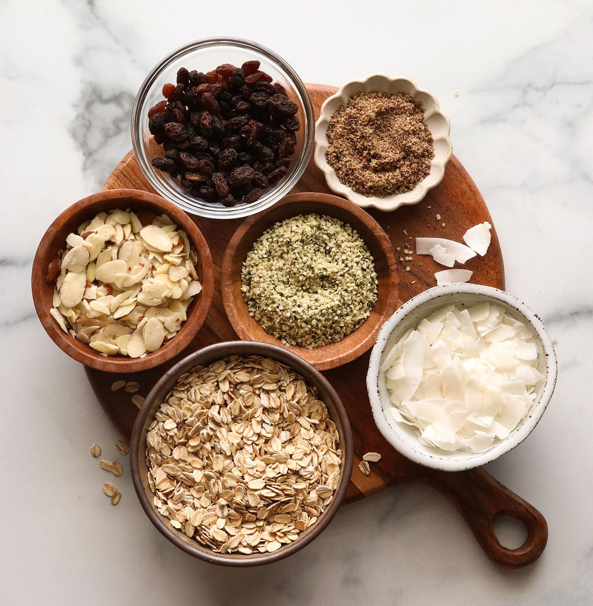 rolled oats, coconut, raisins, hemp hearts, and almonds in separate bowls.