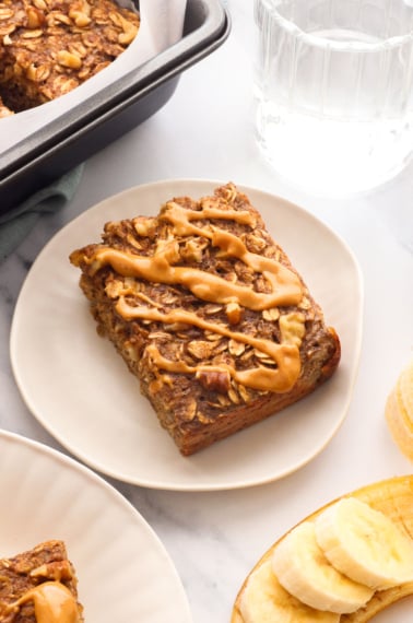 banana baked oatmeal slice with peanut butter on a plate.