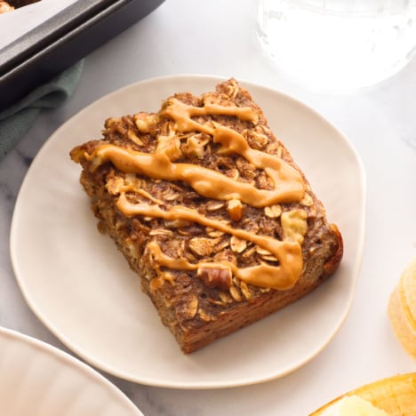 banana baked oatmeal slice with peanut butter on a plate.