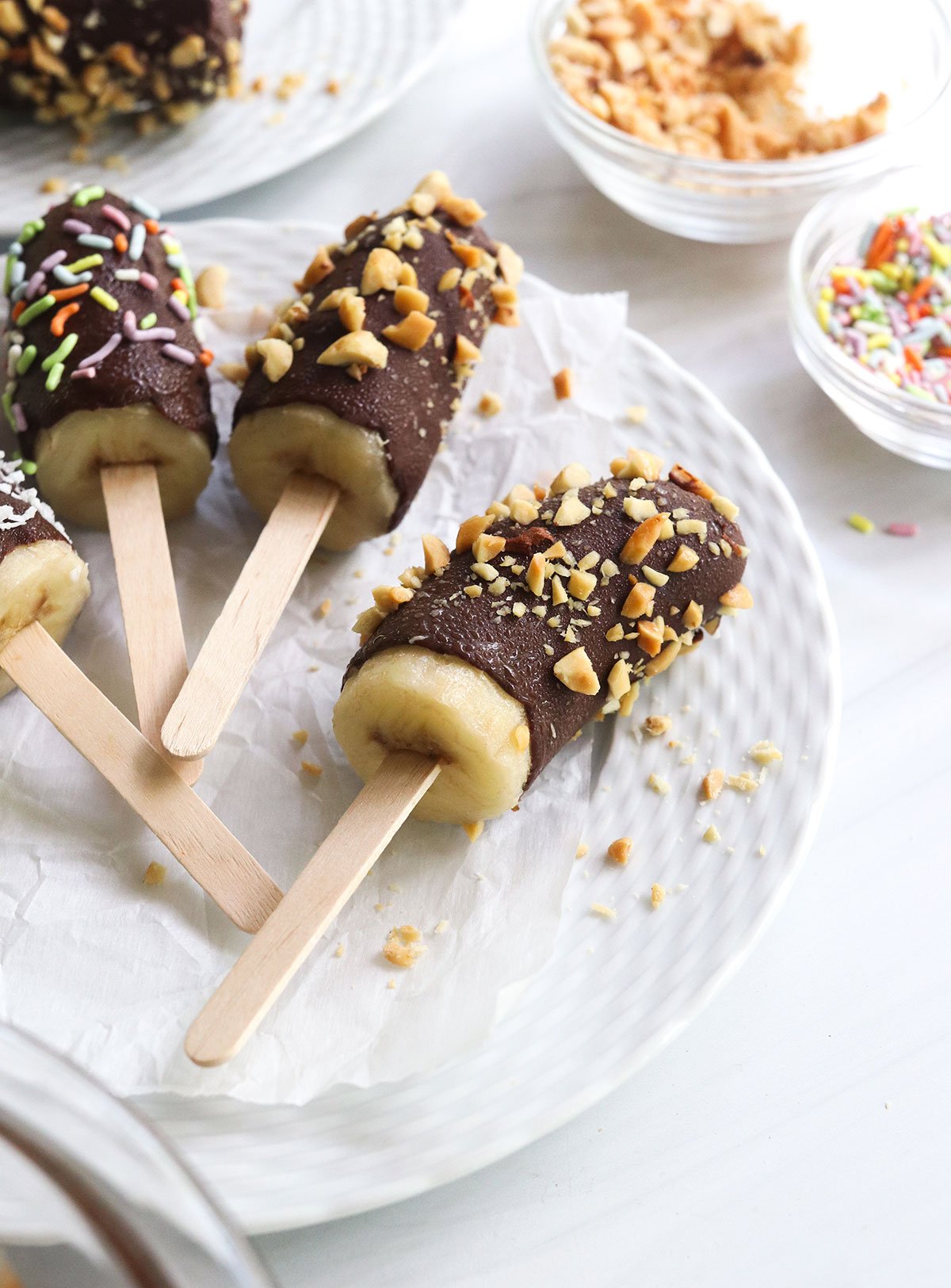 chocolate banana coated in peanuts and sprinkles on a white plate.