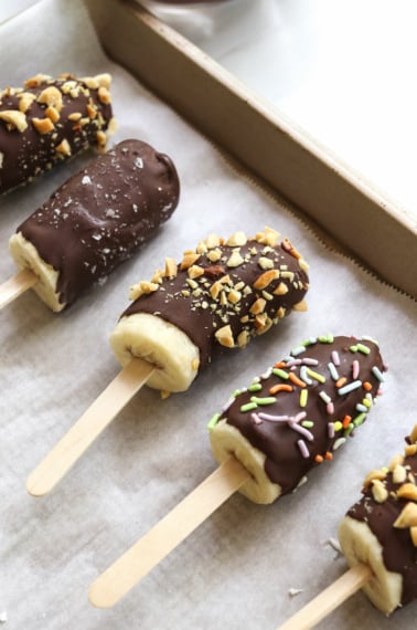 chocolate covered frozen bananas on a parchment lined baking sheet.