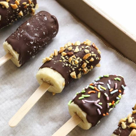 chocolate covered frozen bananas on a parchment lined baking sheet.