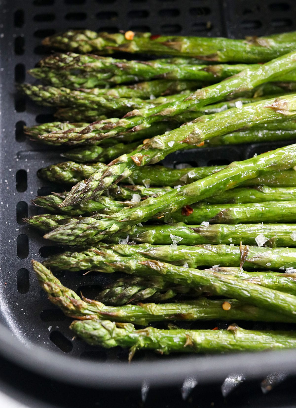 asparagus piled in air fryer basket.