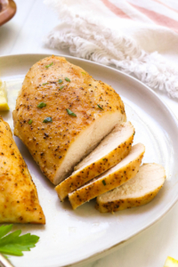 oven baked chicken breast sliced on a white plate with parsley.