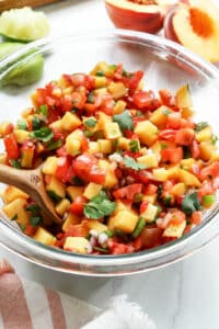 peach salsa in glass bowl with serving spoon.