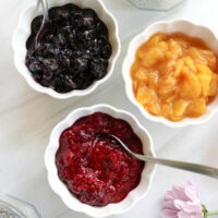 3 different types of fruit compote in bowls with spoons.