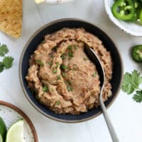 refried beans in a black bowl with serving spoon.