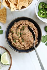 refried beans in a black bowl with serving spoon.