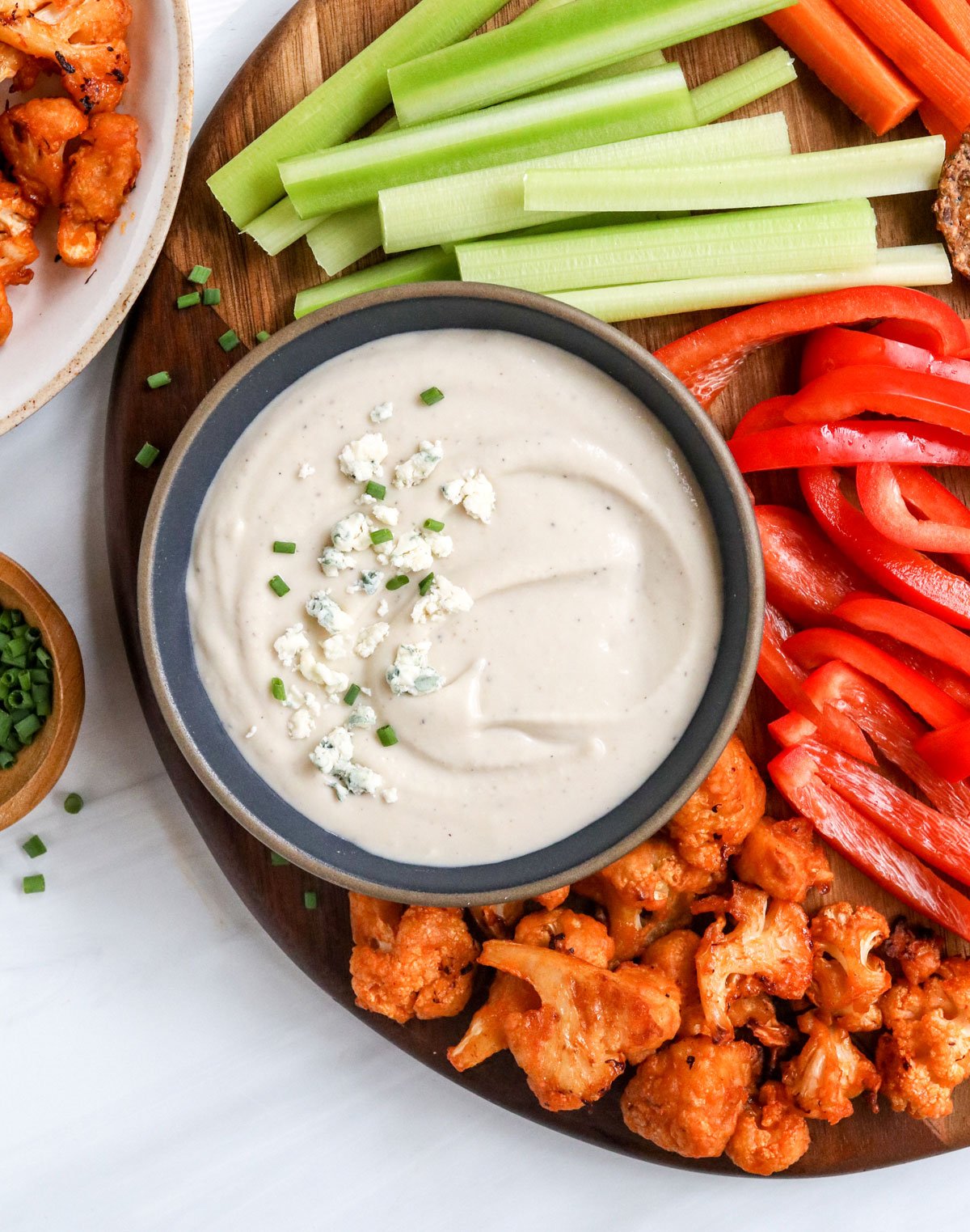 healthy blue cheese dip served with sliced veggies on a cutting board.