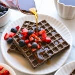 buckwheat waffles with maple syrup poured on top with fruit.