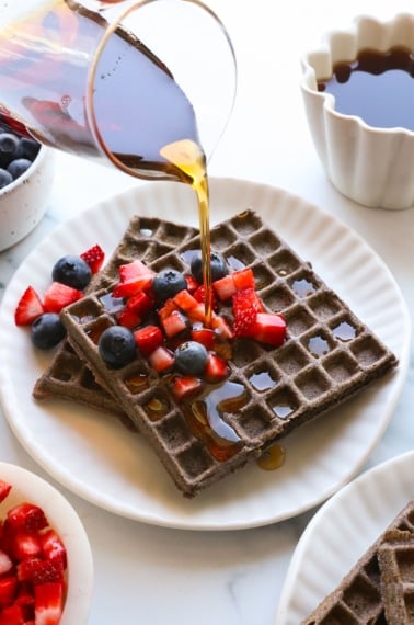 buckwheat waffles with maple syrup poured on top with fruit.