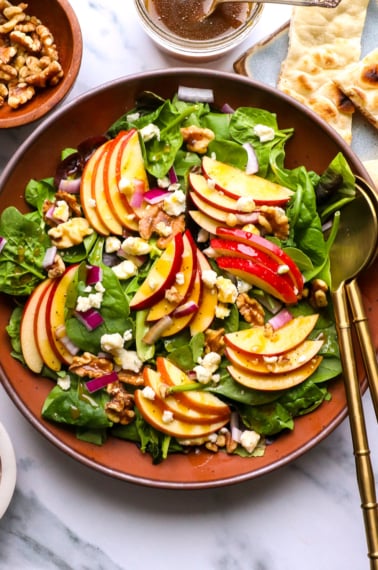 apple walnut salad served with gold tongs and blue cheese.