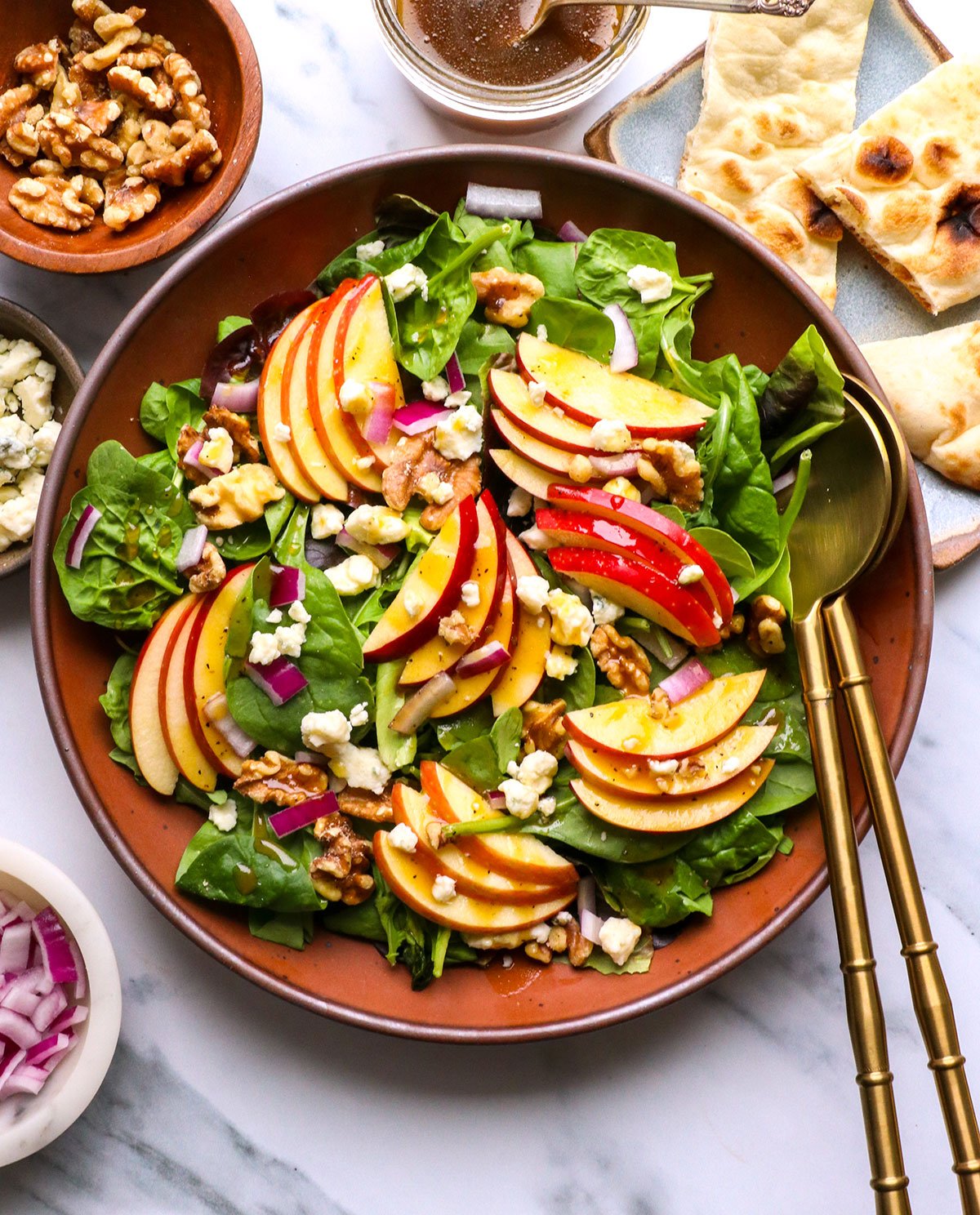apple walnut salad served with gold tongs and blue cheese.