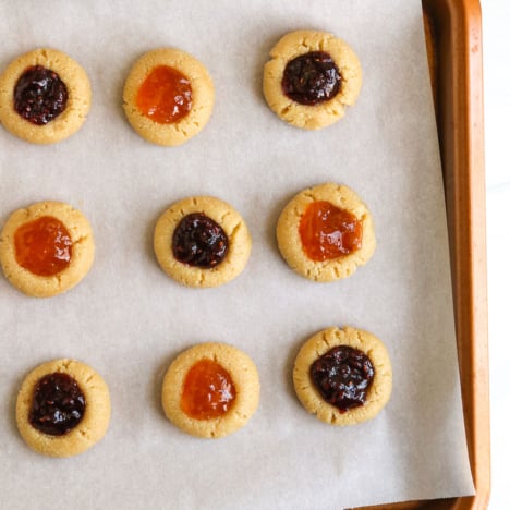 jam added to thumbprint cookies on baking sheet.