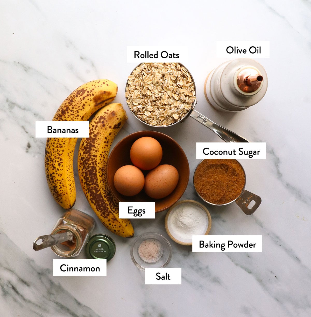 oatmeal, bananas, coconut sugar, olive oil, and spices labeled on a marble surface. 