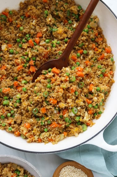quinoa fried rice in white skillet with wooden spoon.