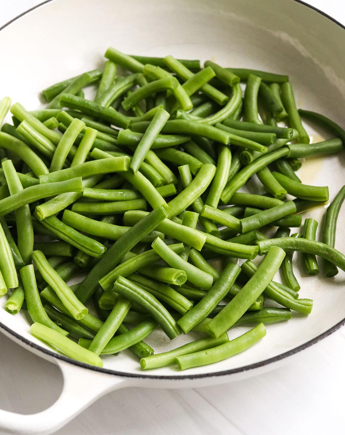 fresh green beans added to a large white skillet.