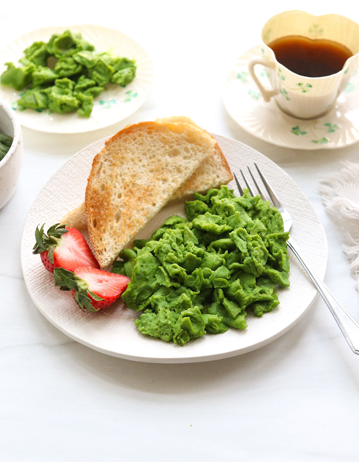 green eggs served on a plate with toast and strawberries.