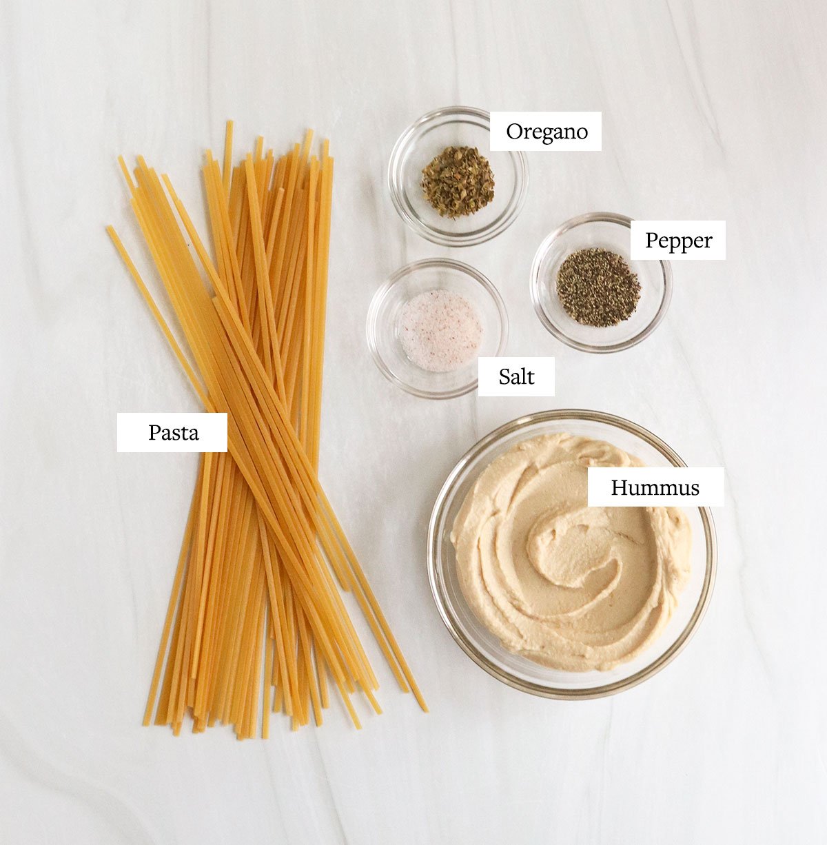 ingredients for hummus pasta labeled on a white surface.