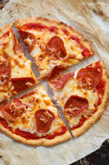 almond flour pizza crust topped with pepperoni and sliced on parchment paper.