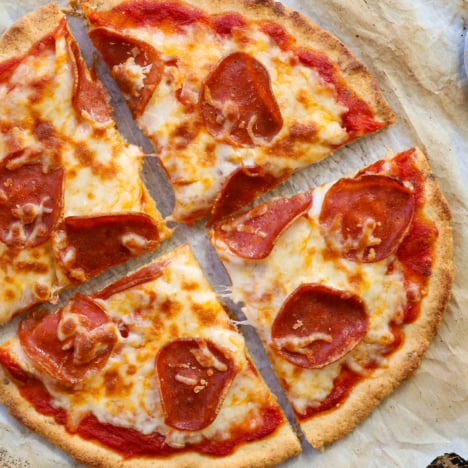 almond flour pizza crust topped with pepperoni and sliced on parchment paper.