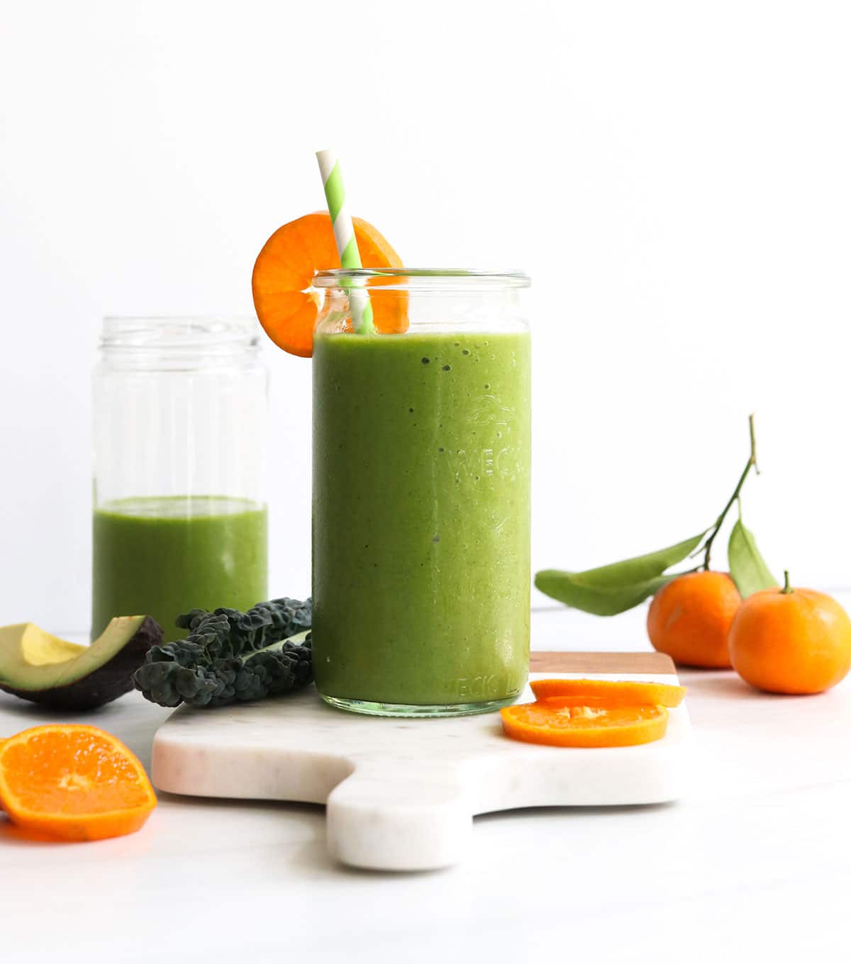 kale smoothie served in two glasses on white marble board.