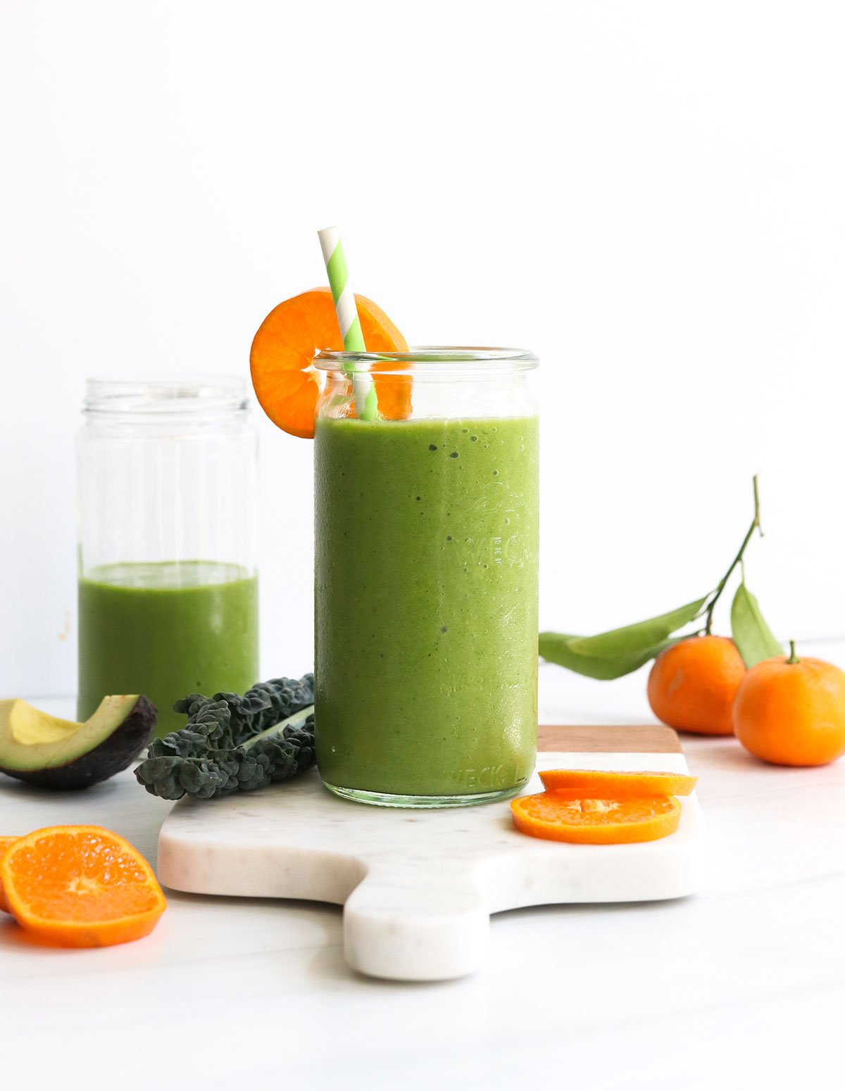 kale smoothie served in glass with an orange slice and straw.