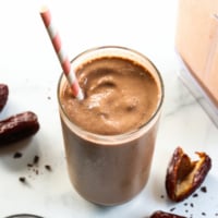 Chocolate date smoothie with a pink straw and dates around it.