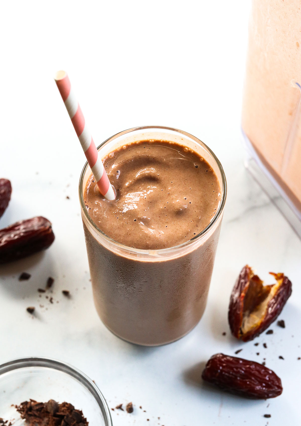 Chocolate date smoothie with a pink straw and dates around it.