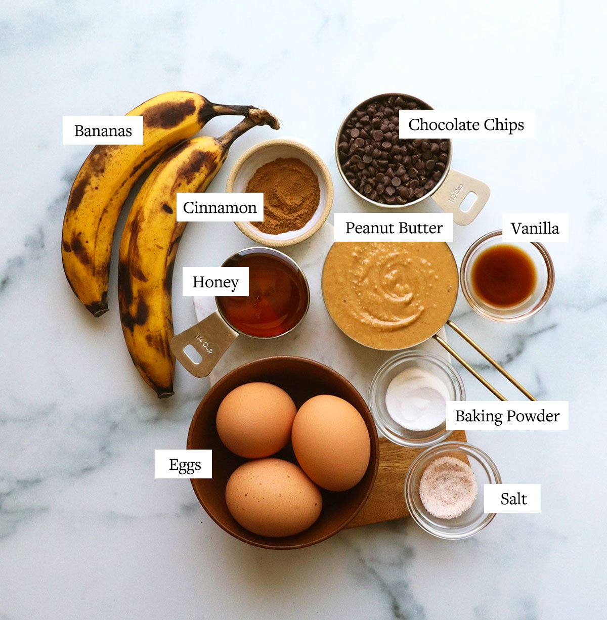 peanut butter, eggs, ripe bananas, and spices labeled on a white surface.