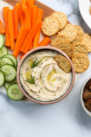 white bean dip topped with rosemary and served with crackers and sliced veggies.