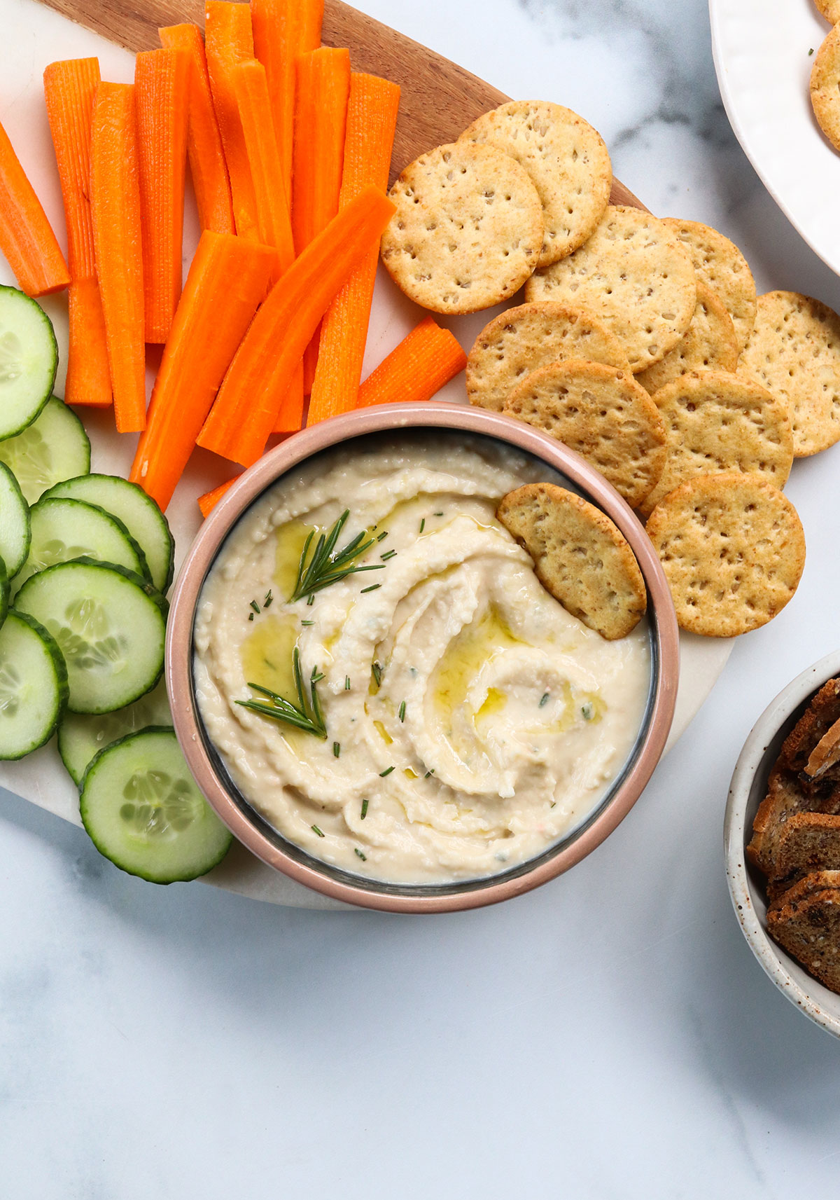 white bean dip topped with rosemary and served with crackers and sliced veggies.