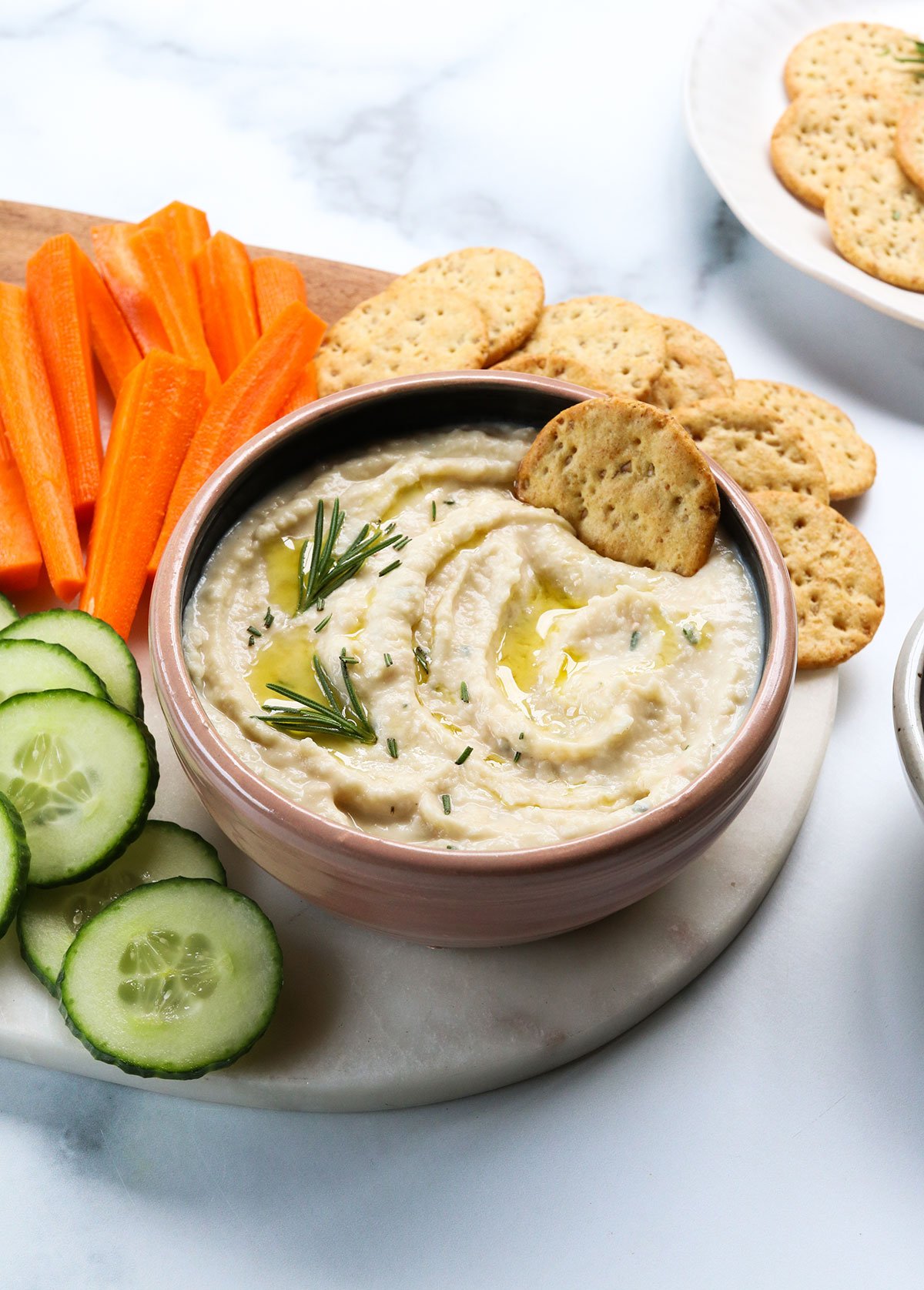 white bean dip served with crackers and sliced veggies on a platter.