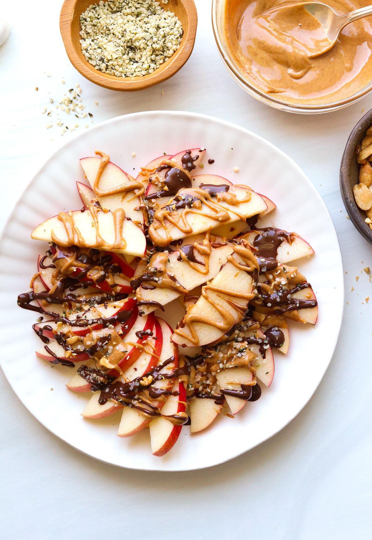 apple nachos served on a white plate with peanut butter and melted chocolate drizzle.