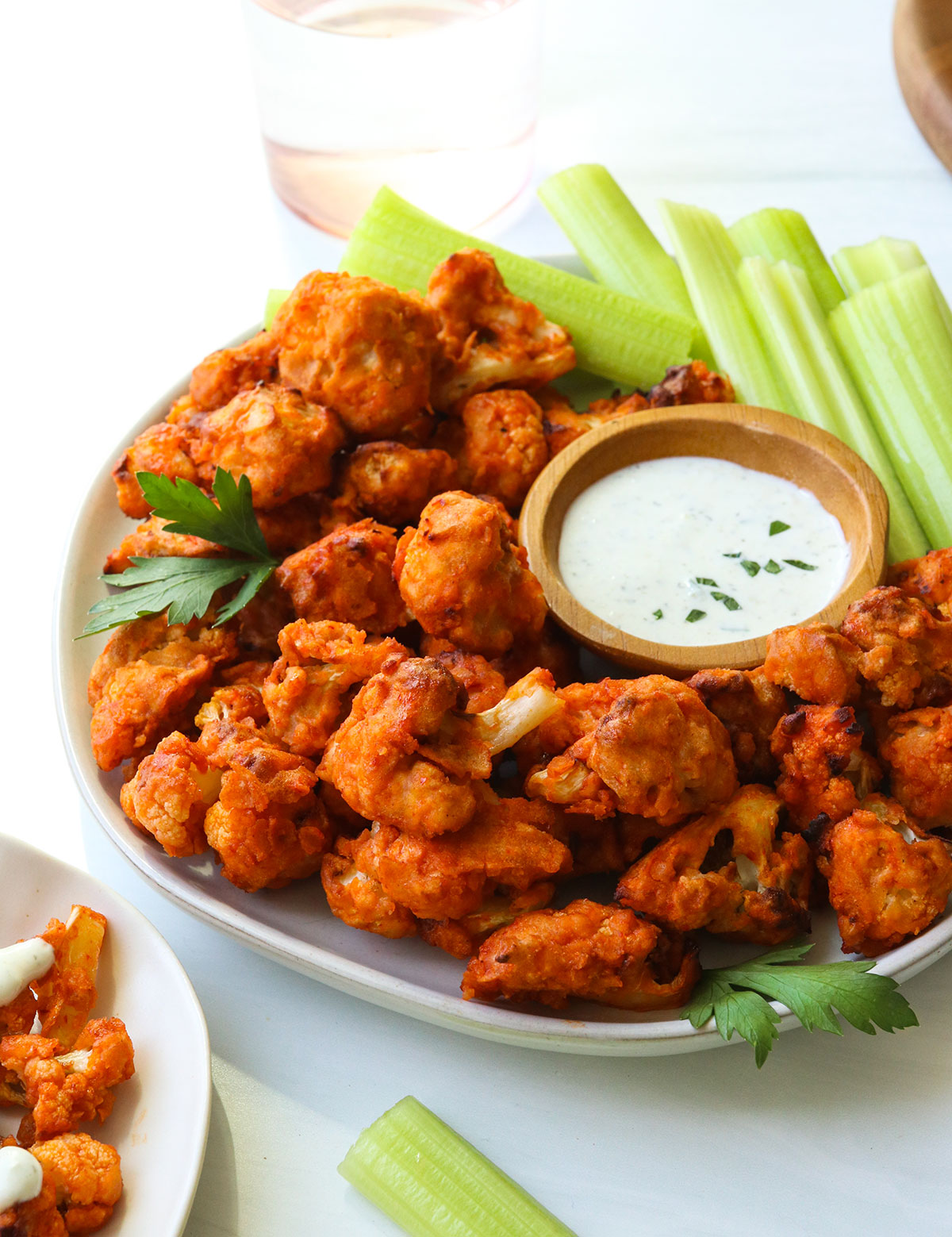 buffalo cauliflower served on a white plate with celery and ranch dip.