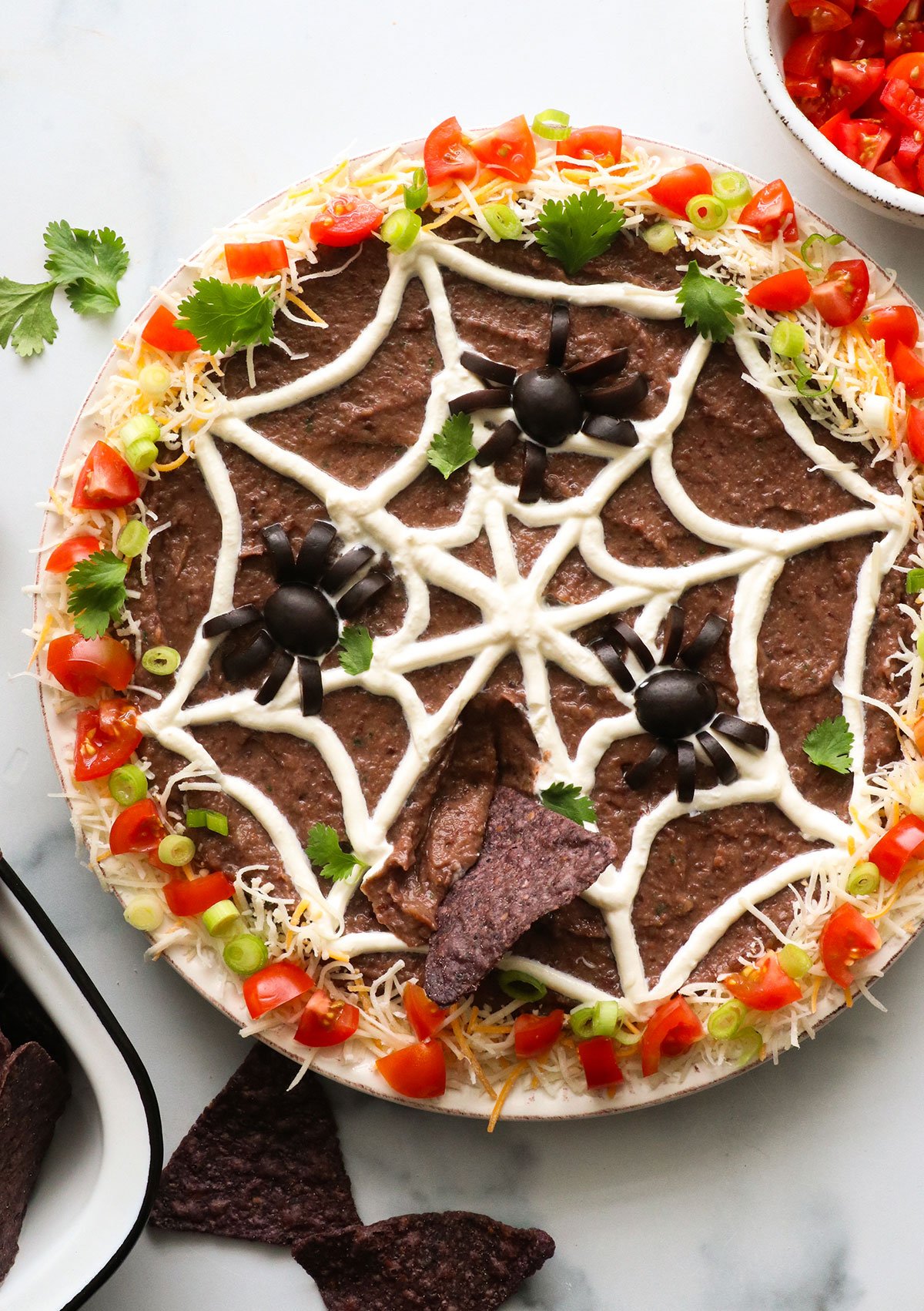 bean dip with a sour cream spider web and black olive spiders on top.