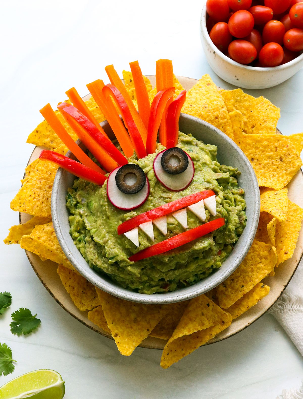 bowl of guacamole decorated with veggies to look like a monster face.