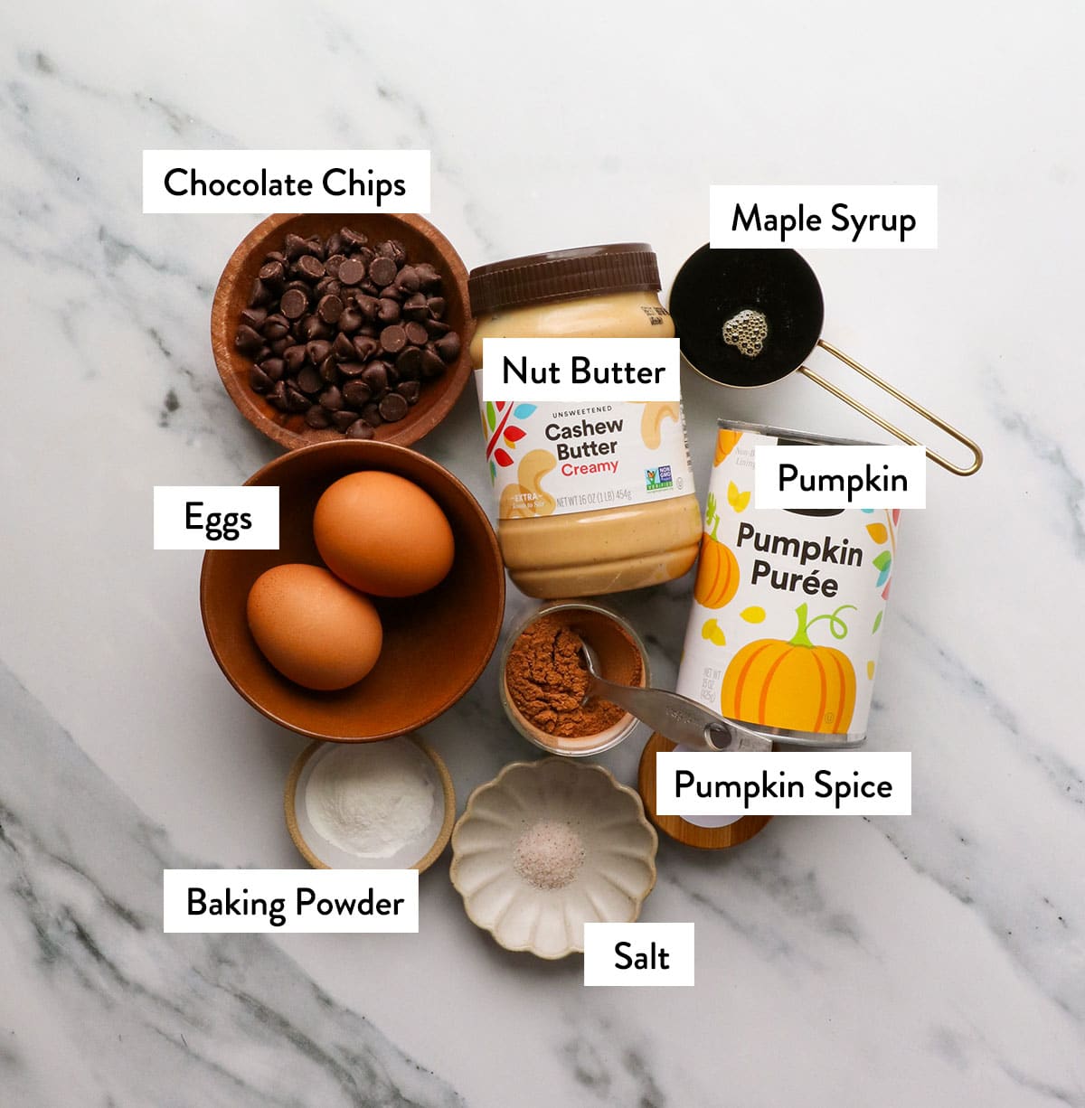 cashew butter, eggs, pumpkin puree, maple syrup, and spices on a white surface.