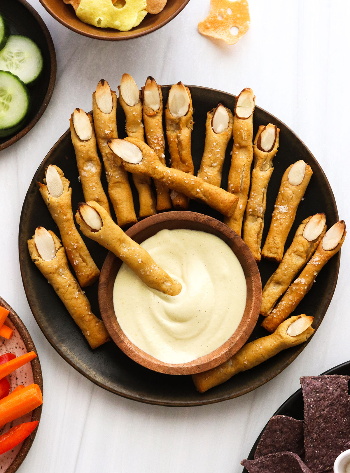 A dark plate filled with witch finger shaped pretzels and cheese dip.