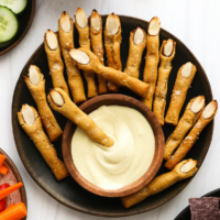 Witch finger pretzels on a black plate with cheese dip.