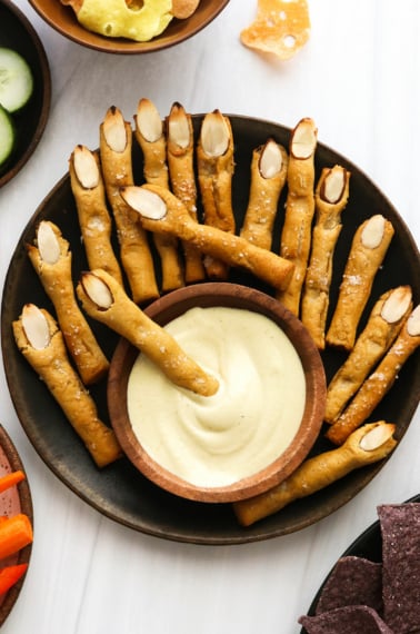 Witch finger pretzels on a black plate with cheese dip.