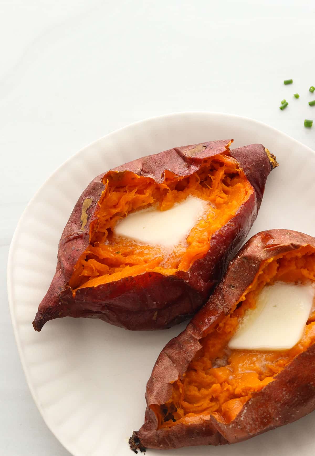 two baked sweet potatoes on a white plate topped with butter.