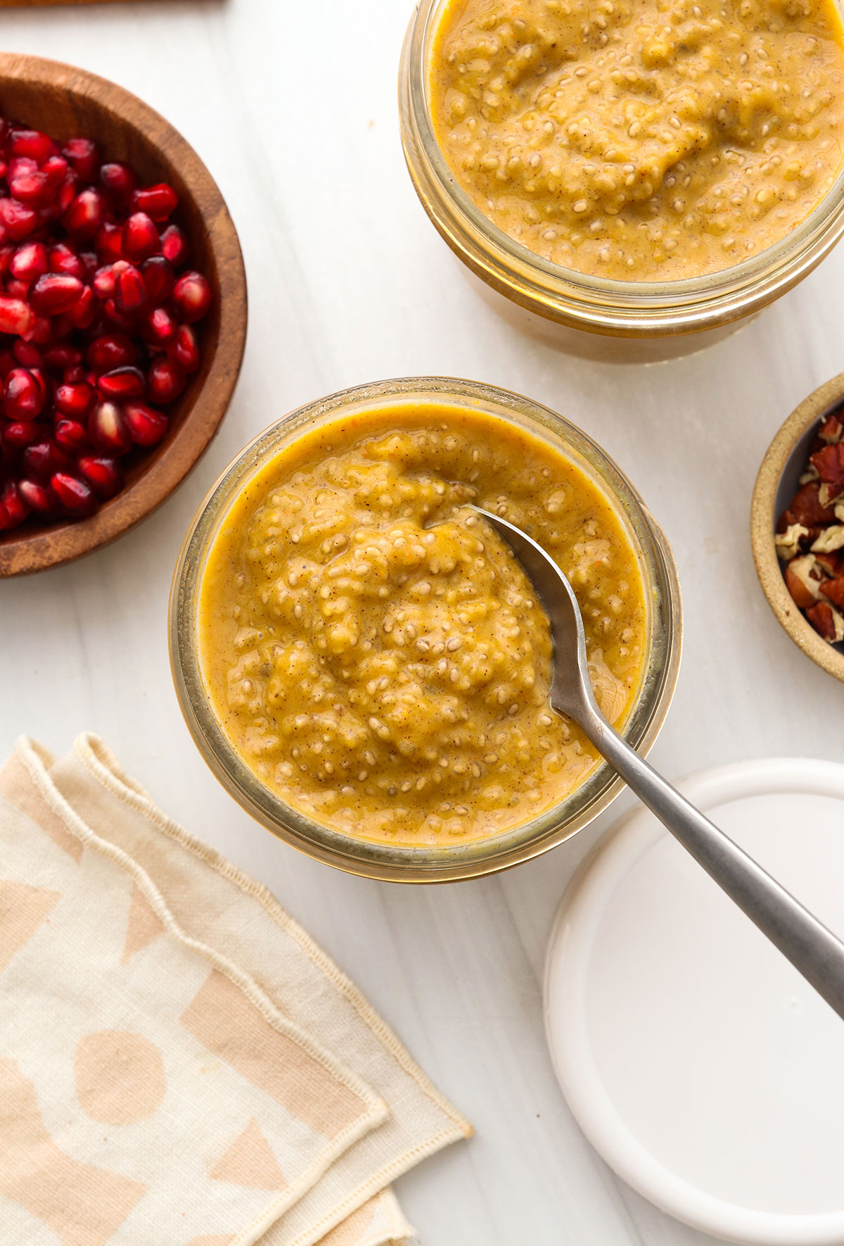 pumpkin chia pudding in two glass jars with a spoon.