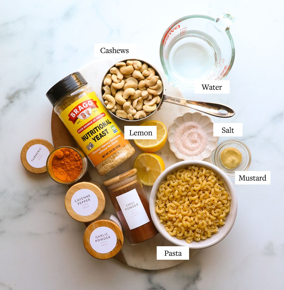 bowls of cashews, noodles, spice jars, and a bottle of nutritional yeast on a marble board. 