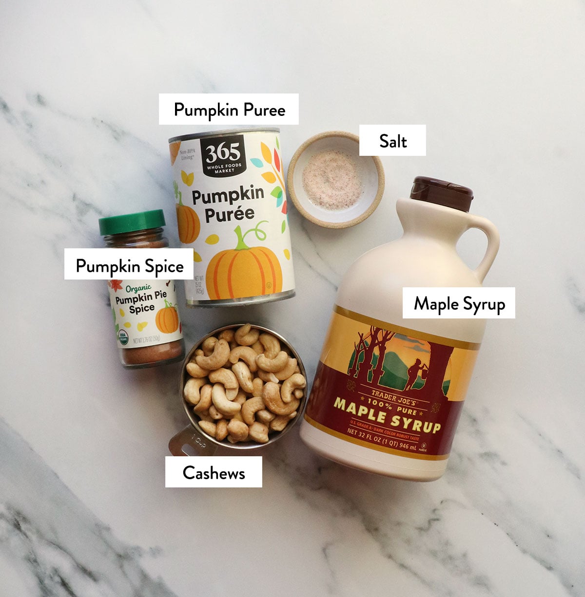 cashews, pumpkin can, maple syrup, pumpkin pie spice, and salt labeled on a white surface.