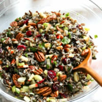 wild rice salad served in a large glass bowl with wooden spoon.