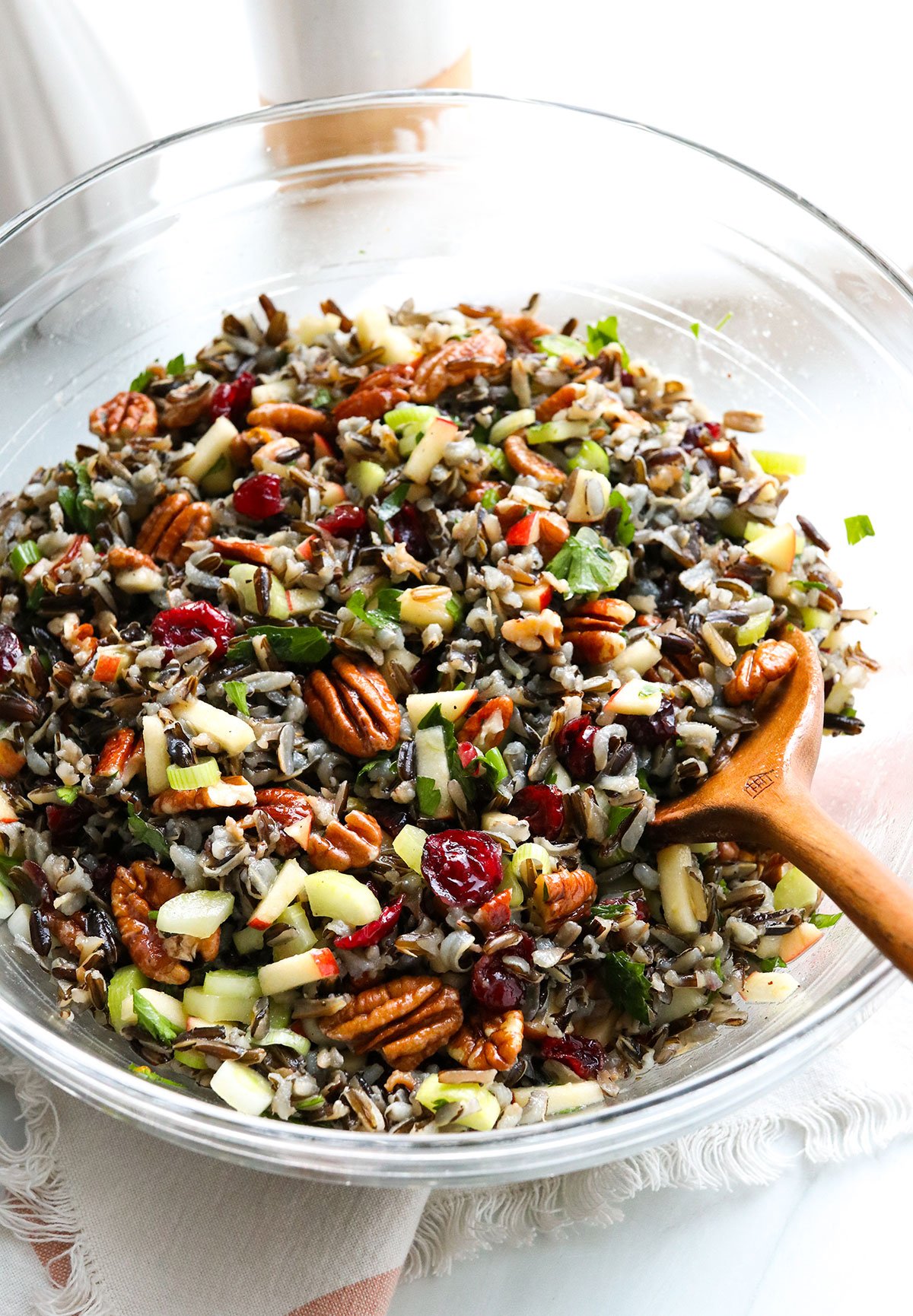 wild rice salad served in a large glass bowl with wooden spoon.