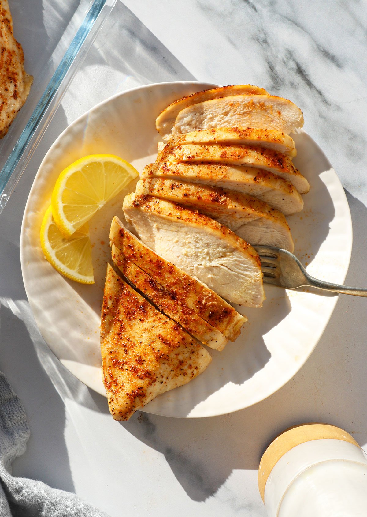 baked chicken breast sliced on a white plate with lemon slices nearby.  - 2