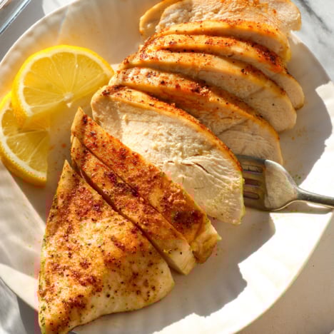 close-up of sliced oven baked chicken breast on a white plate with lemon slices.