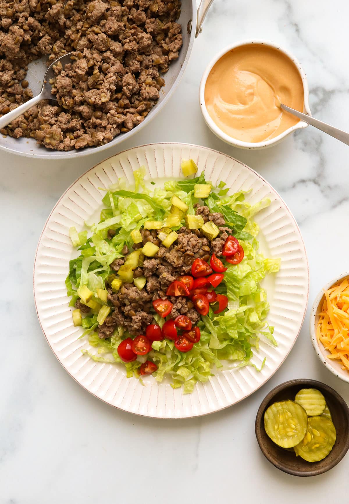 salad topped with burger crumbles, diced pickles, tomatoes, and sauce on the side.